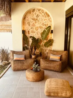 a patio with three wicker chairs and a stone wall at Naya pool & garden view bungalow in Koskinou