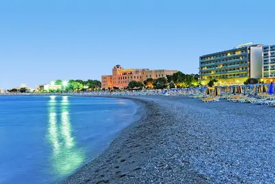 a beach with chairs and buildings and the water at Mediterranean Hotel in Rhodes Town