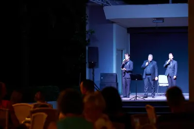 three men standing on a stage in front of a crowd at Apollo Beach in Faliraki
