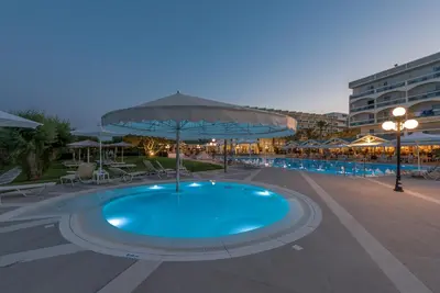 a swimming pool with an umbrella and chairs and a building at Apollo Beach in Faliraki