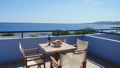 a table with a bottle of wine and a bowl of fruit on a balcony at Paraktio Beach Apartments in Kiotari