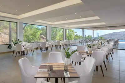 a restaurant with white chairs and tables and windows at Lindos Village Resort & Spa - Adults Only in Líndos