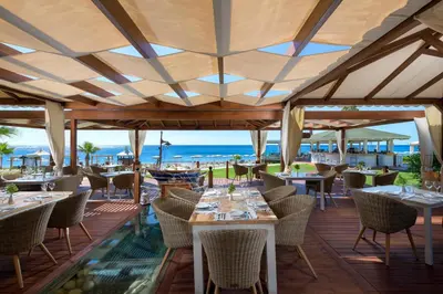 a restaurant with tables and chairs and the ocean in the background at Rodos Palladium Leisure & Wellness in Faliraki