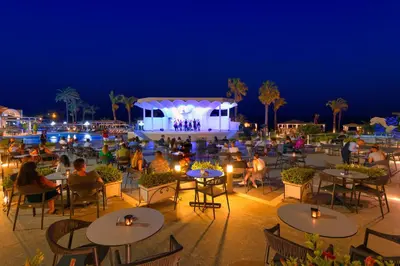 a group of people sitting at tables at a pool at night at Rodos Palladium Leisure & Wellness in Faliraki