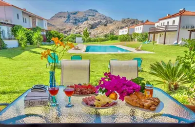 a table with plates of food and drinks and a pool at Posidonia Luxury Villas Kolympia in Kolimbia