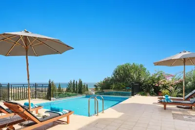 a swimming pool with two chairs and umbrellas at Villa Petalouda by Villa Plus in Kalathos