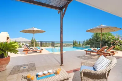 a patio with chairs and umbrellas and a pool at Villa Petalouda by Villa Plus in Kalathos