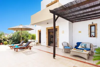 an outdoor patio with chairs and an umbrella at Villa Petalouda by Villa Plus in Kalathos