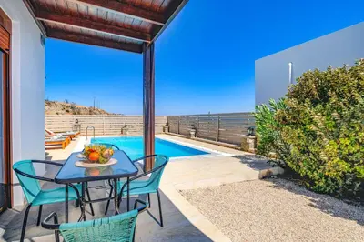 a patio with a table and chairs and a swimming pool at Villa Kiotari by Villa Plus in Kiotari