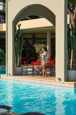 a woman standing on a porch next to a swimming pool at Dionysos Hotel in Ixia
