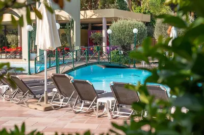a group of chairs and umbrellas next to a pool at Dionysos Hotel in Ixia