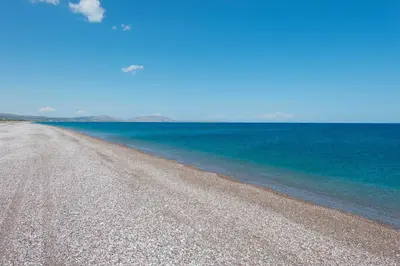 a beach with blue water and a gravel road at Villa Amelia in Gennadi