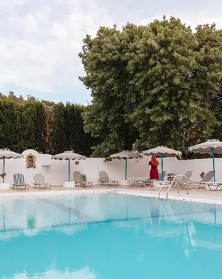 a woman walking by a swimming pool with chairs and umbrellas at Hotel Nathalie in Ixia