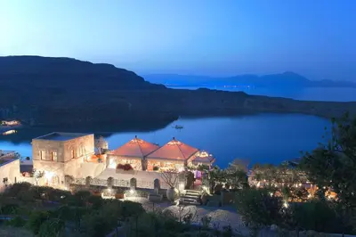 a large building with lights in front of a lake at Melenos Art Boutique Hotel in Líndos