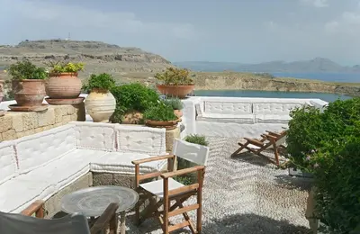a patio with chairs and potted plants and water at Melenos Art Boutique Hotel in Líndos