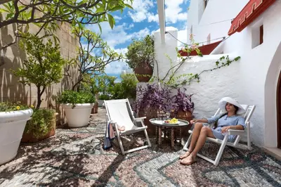 a woman sitting in a chair on a patio at Melenos Art Boutique Hotel in Líndos