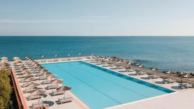 a swimming pool with chairs and umbrellas and the ocean at Eden Roc Resort - All Inclusive in Kallithea Rhodes