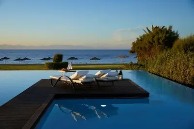 a pool with chairs and a table and the ocean at The Ixian Grand & All Suites - Adults Only Hotel in Ixia