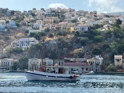 a boat in the water in front of a city at Aleminas Rooms 1 in Symi
