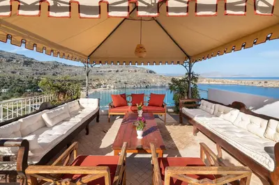 a patio with couches and tables and a view of the water at Villa Venetoklis in Líndos
