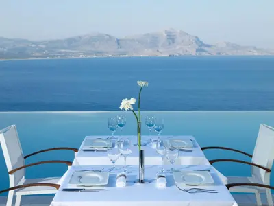 a table with wine glasses and a vase with a flower at Lindos Blu Luxury Hotel-Adults only in Líndos