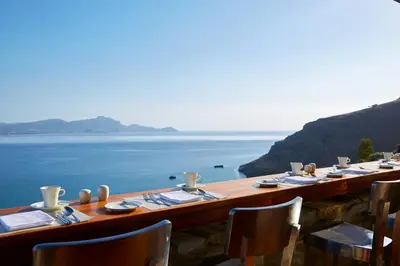 a long wooden table with a view of the ocean at Lindos Blu Luxury Hotel-Adults only in Líndos