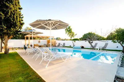 a swimming pool with chairs and an umbrella at Villa Eleni in Soroni