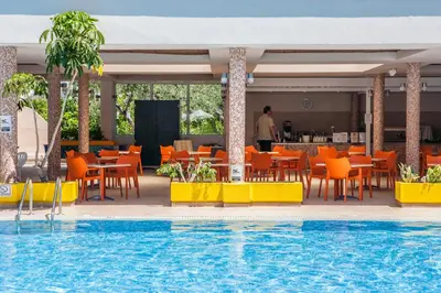 a pool at a hotel with orange chairs and tables at IALYSSOS BAY HOTEL in Ialyssos
