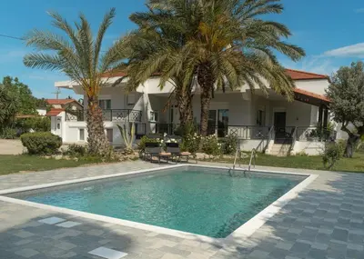 a swimming pool in front of a house with palm trees at Propodes Luxury Villa in Pastida