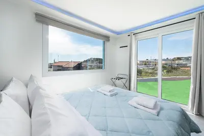a white bedroom with a bed and a large window at GR House Eleftheria in Afantou