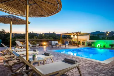 a villa with a swimming pool with chairs and an umbrella at Villa Merelia in Afantou