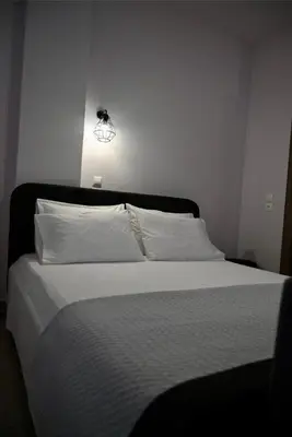 a bed with white sheets and a light on the wall at Casa Sym Faliraki in Faliraki